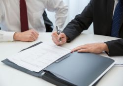 a person in black suit holding a pen near the documents on the table